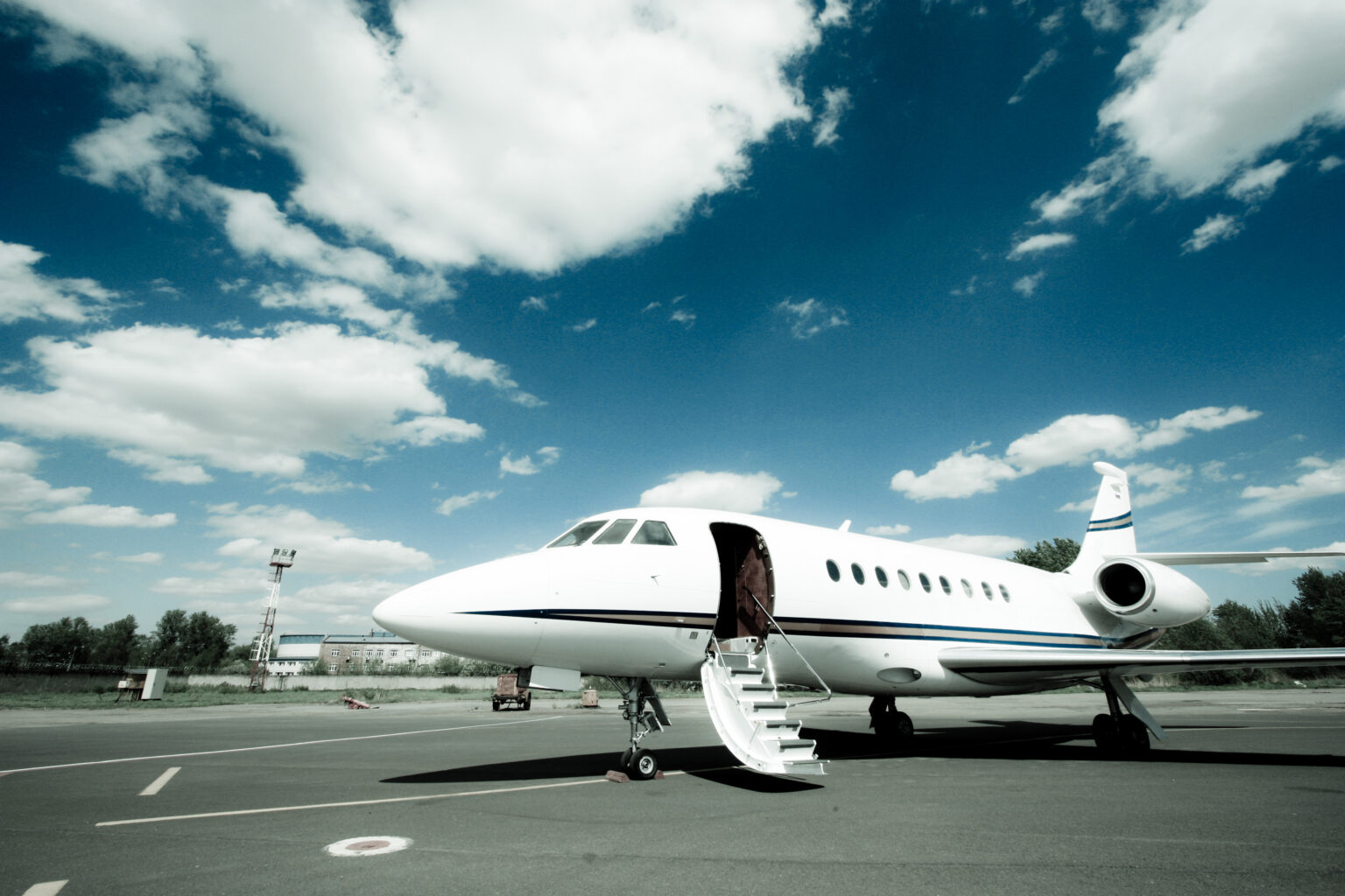 A midsize business jet parked on the ramp with its airstair door lowered, waiting for passengers under a blue sky.