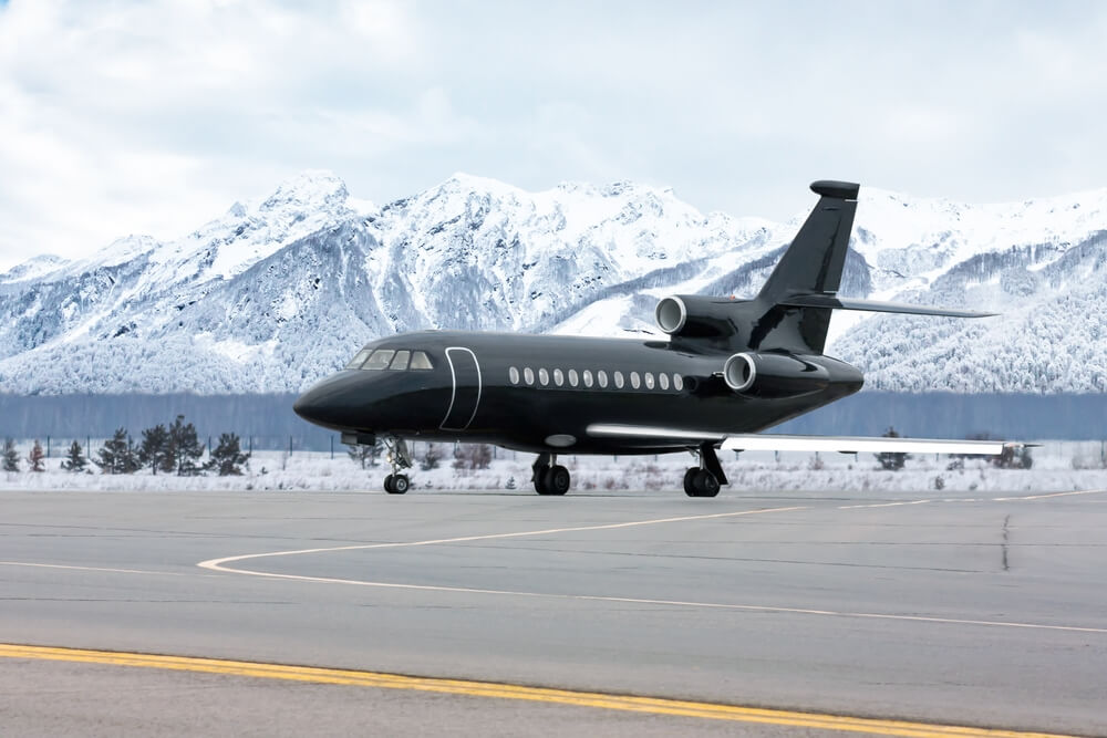 A private jet taxiing at a mountain airport with snow-covered peaks behind it at the start of ski season.