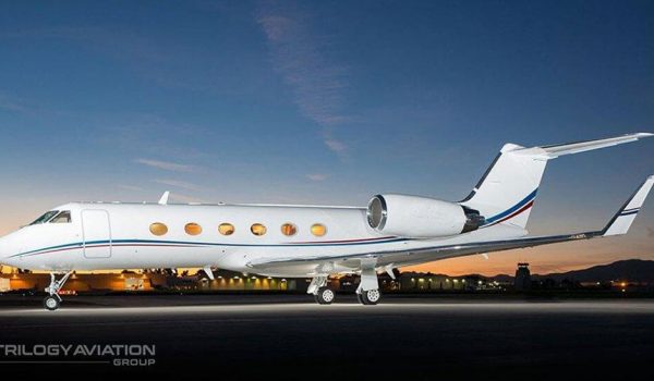 A sleek white Gulfstream G450 private jet parked on a tarmac at sunset, ready for departure from Dallas.